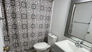 Un baño con cortina de ducha estampada, inodoro blanco, lavamanos con espejo y suelo de baldosas.