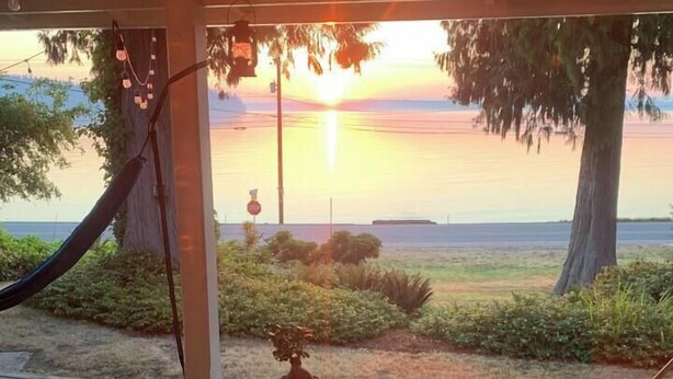 A wooden deck with white chairs and a table, overlooking a sunset over a body of water. - Beachside Escape w/ Kayaks | Access to Seattle (Port Orchard)