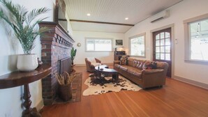 A spacious living room with a brick fireplace, leather sofa, and a large window providing natural light. - Beachside Escape w/ Kayaks | Access to Seattle (Port Orchard)