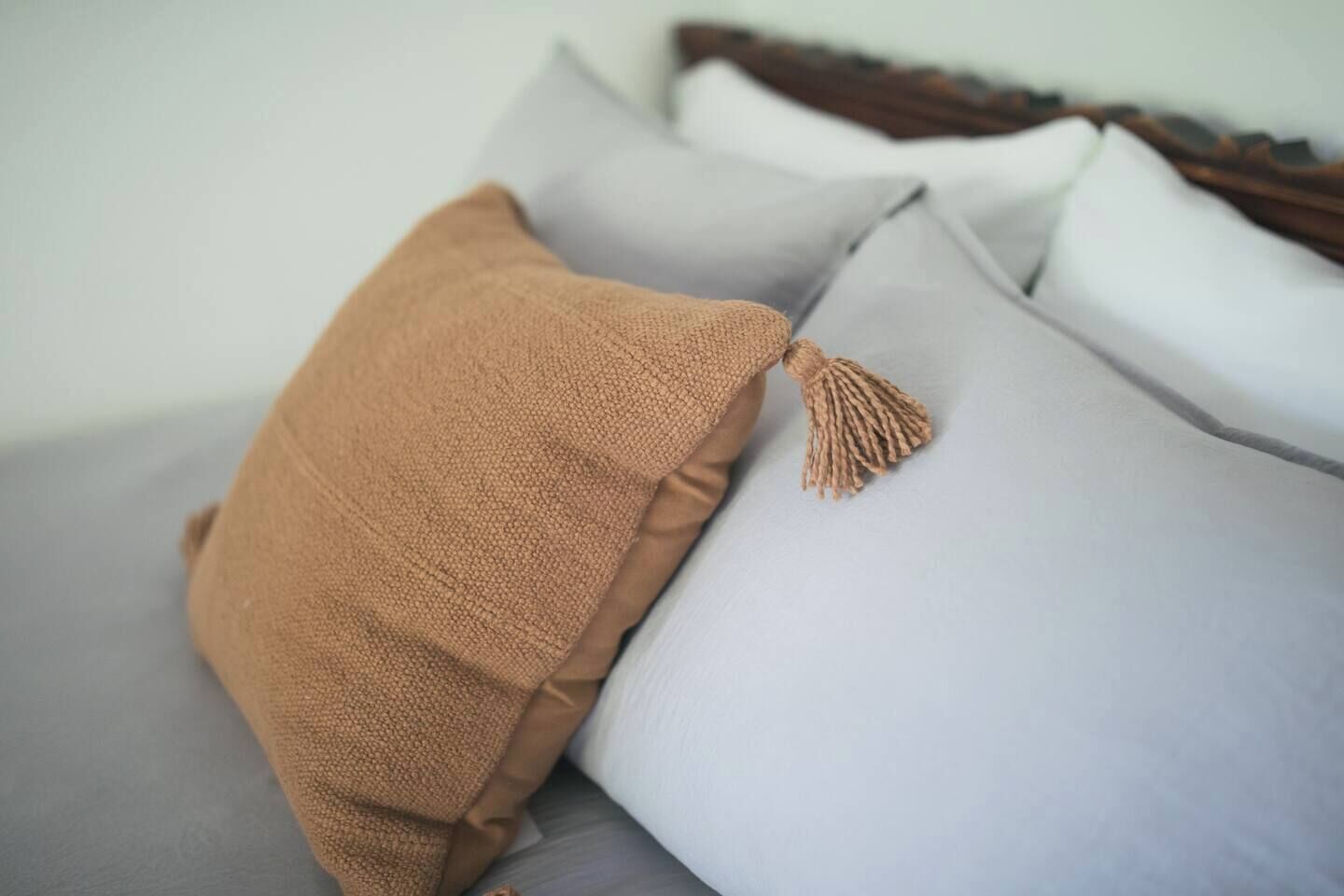 A bed with a brown blanket and a white pillow with a tassel.