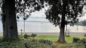 A landscaped area with trees and shrubs, a stop sign, and a view of a body of water with boats. - Beachside Escape w/ Kayaks | Access to Seattle (Port Orchard)