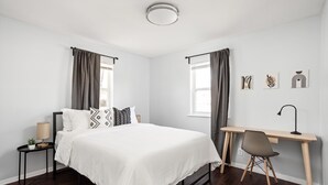 Ein modernes Schlafzimmer mit Bett, Schreibtisch, Stuhl und Bildern an der Wand.