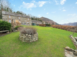 A stone house with a stone staircase, a well-maintained lawn, and a mountain in the background.