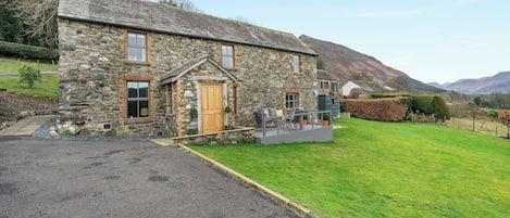 A stone house with a wooden door, a porch, and a grassy yard.