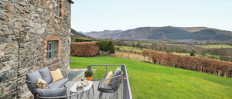 Un edificio de piedra con terraza, mobiliario exterior y vistas a un campo y montañas.