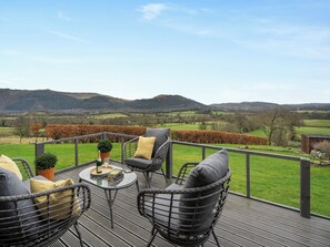 Una terrazza con sedie in vimini e un tavolo, affacciata su un paesaggio rurale con campi e colline.