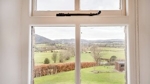 Una ventana con vistas a un paisaje rural, que incluye campos, árboles y colinas a lo lejos.