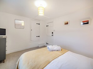 Ein Schlafzimmer mit Bett, Nachttisch, Fernseher, Tür und einer Lampe.