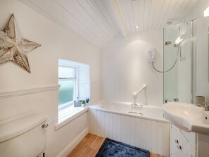 A bathroom with a white bathtub, a white sink, a glass shower enclosure, a star decoration on the wall, and a window with a view.