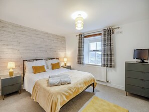A bedroom with a bed, bedside lamps, a dresser, a television, and a window with curtains.