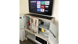 Un televisor montado en un estante de madera rústica con diversos objetos como una cafetera y una taza.