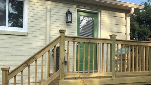 Una escalera de madera que lleva a una puerta verde con un farol encima.