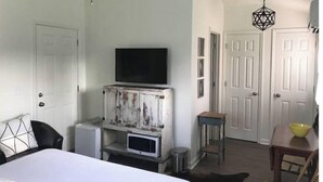 Un dormitorio con una cama, un televisor sobre un mueble de madera, un ventilador de techo y una puerta.