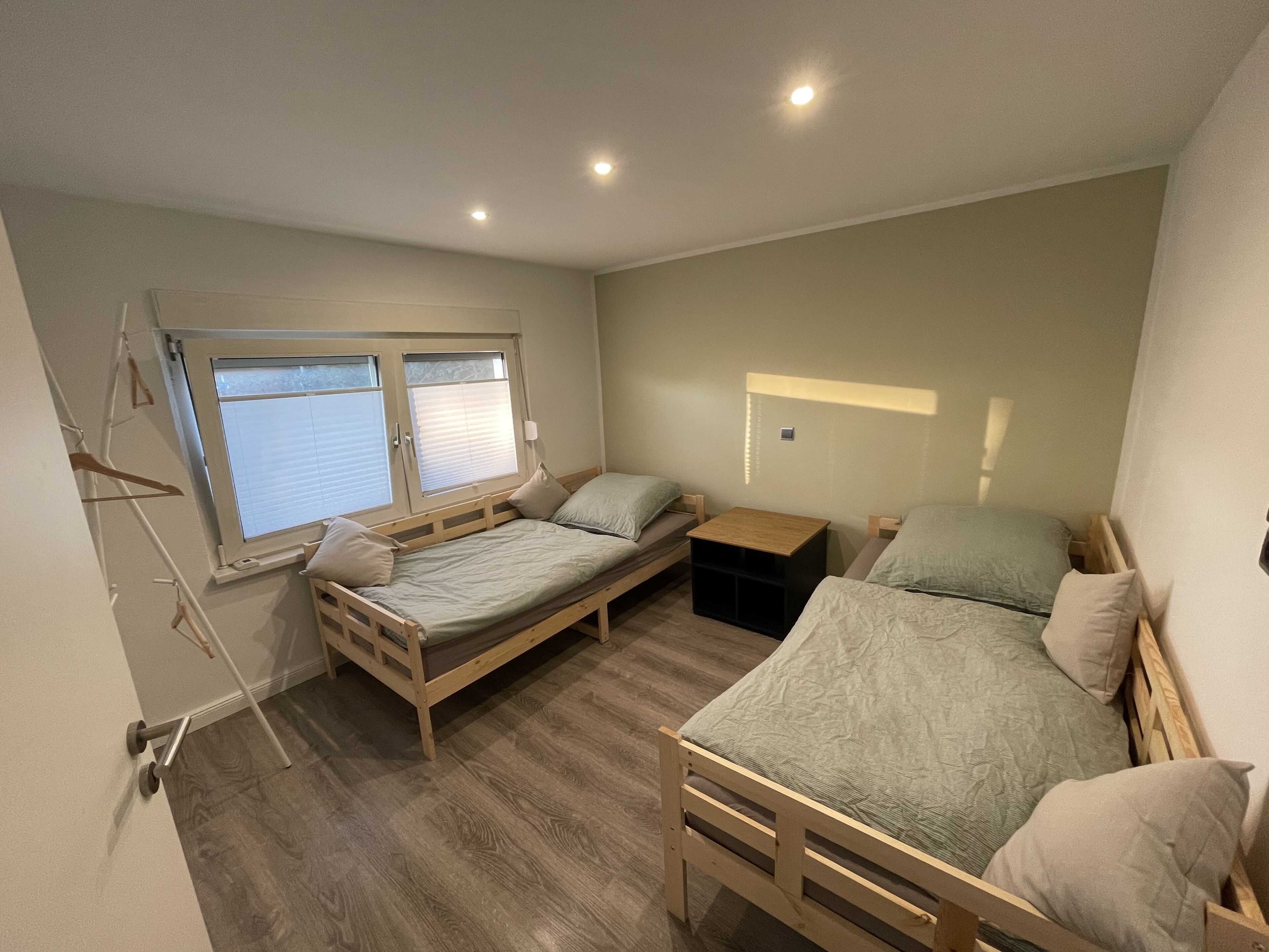 A compact room with two wooden beds, a small wooden nightstand, and a window with blinds.