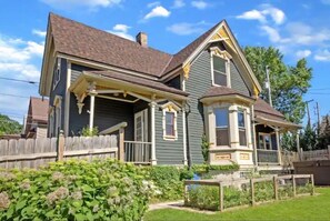 Une maison à deux étages avec un porche, un petit jardin et une clôture en bois.