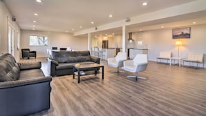 A spacious living area with a leather sofa, a coffee table, and white chairs. A kitchen is visible in the background. - Fully Remodeled Hillsboro Home w/ Home Theater! (Hillsboro)