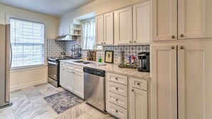 A kitchen with white cabinets, a stainless steel dishwasher, a window with blinds, and a tiled backsplash. - Little Rock Home ~ 5 Mi to Downtown! (Little Rock)