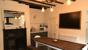 Une cuisine moderne avec une table en bois, des chaises blanches, un tableau noir et une cheminée.