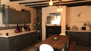 Une cuisine moderne avec des meubles de couleur sombre, une table en bois et une chaise blanche. On y trouve une cheminée en pierre, un four à micro-ondes et une machine à café sur le plan de travail.