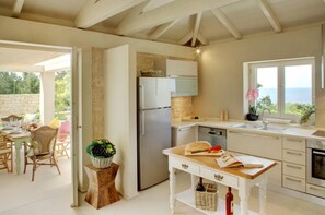 Une cuisine moderne équipée d’un four encastré, d’un réfrigérateur et d’un coin repas avec des chaises et une table en osier.