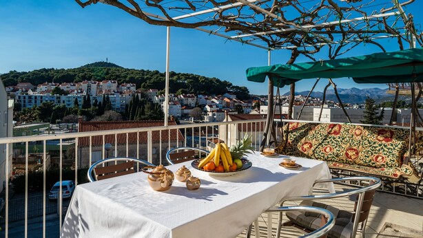 Une terrasse avec une table dressée pour le dîner, offrant une vue sur une ville située sur une colline.