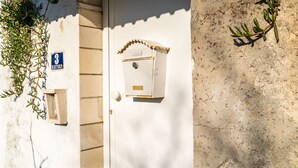 Une porte blanche avec une boîte aux lettres et une petite fenêtre. Un panneau indiquant le numéro « 3 » est fixé au mur, sur la gauche.