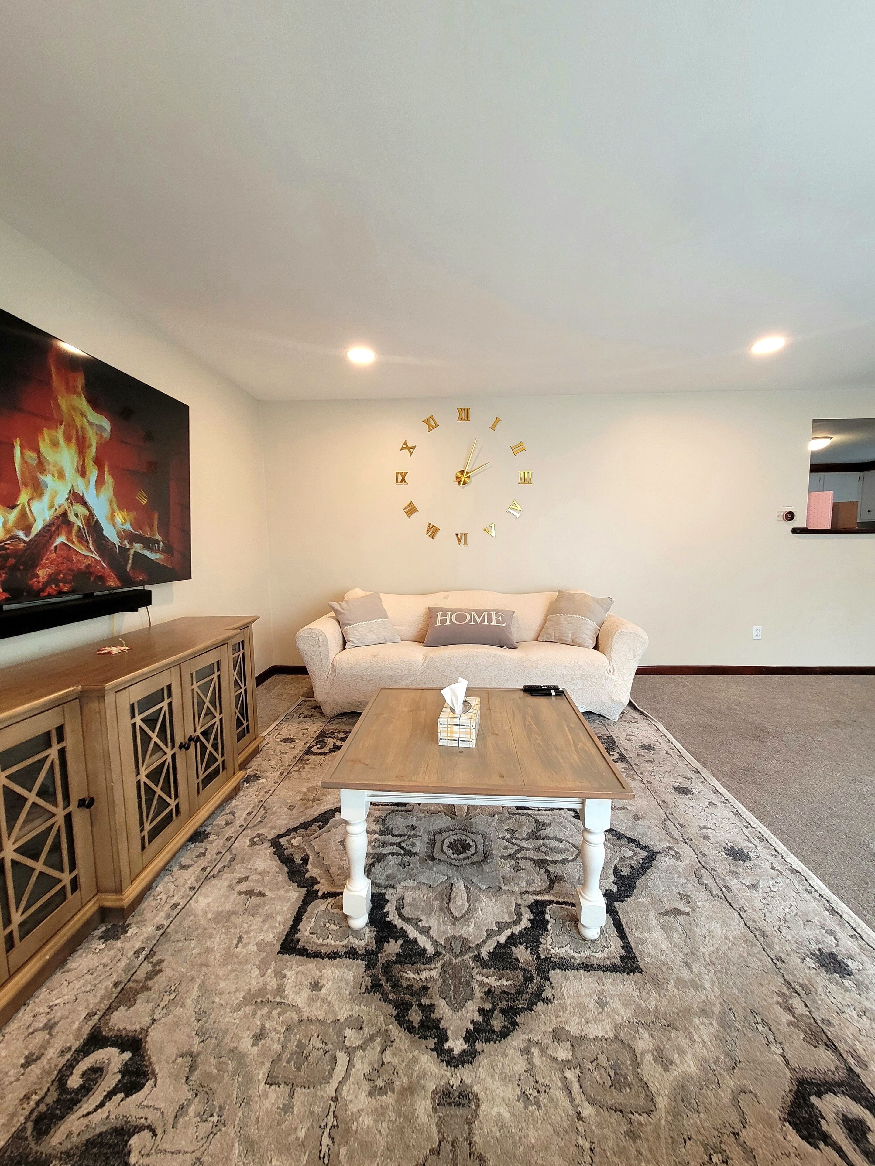 Una sala de estar con sofá, mesa de centro, televisor, reloj y alfombra estampada.