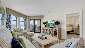 A spacious living room with a sofa set, a coffee table, and a TV. There is a balcony with a view of the sea. - 417 Seascape by Avantstay Beachfront Condo w/ Communal Pool Access (Isle of Palms)