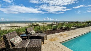 A poolside area with wicker furniture and a view of the ocean.