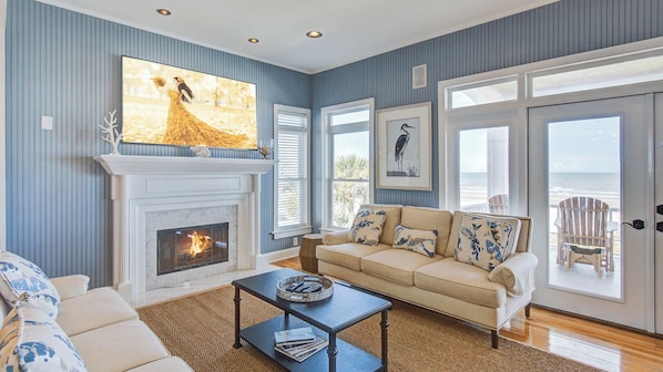 A living room with a fireplace, a sofa, a coffee table, and a view of the ocean through large windows.