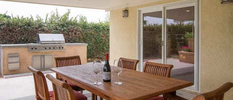 Un patio al aire libre con mesa y sillas de madera, una parrilla y una botella de vino.