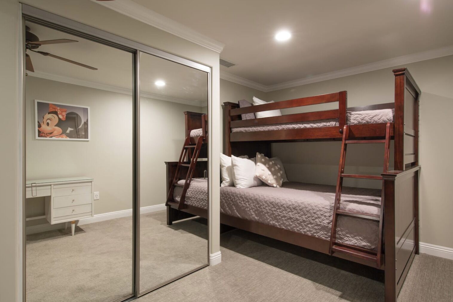 A bedroom with a bunk bed, a desk, and a mirror.