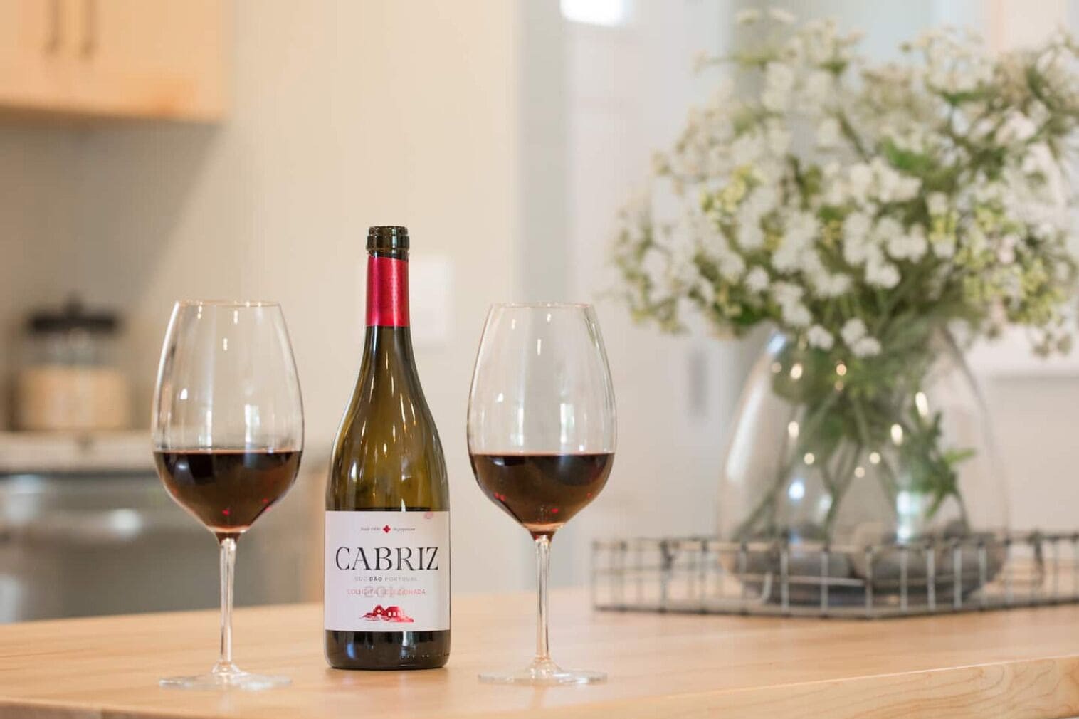 A bottle of Cabriz wine with two glasses of red wine on a wooden table.