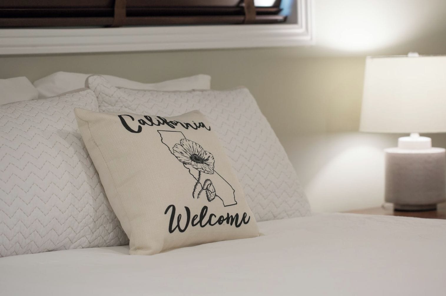 A bed with pillows, one of which has a design featuring the state of California and the word "Welcome".