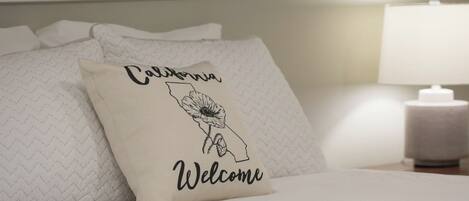 A bed with pillows, one of which has a design featuring the state of California and the word "Welcome".