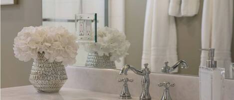 A bathroom with a white sink, two faucets, a mirror, and a vase with white flowers.