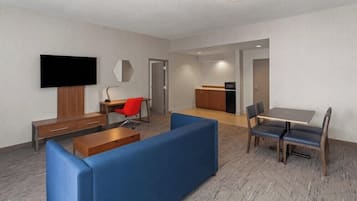 Una moderna camera d'albergo con un divano, un tavolo da pranzo con sedie, una TV a parete e un angolo cottura.