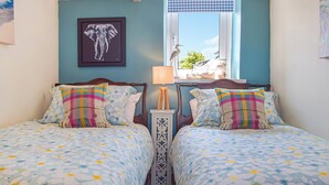 A bedroom with two beds, floral bedding, a framed elephant picture, a window with a view, and a decorative window valance. - Picked for its character, charm and gorgeous sea views from every window. (Berea, near St Davids)