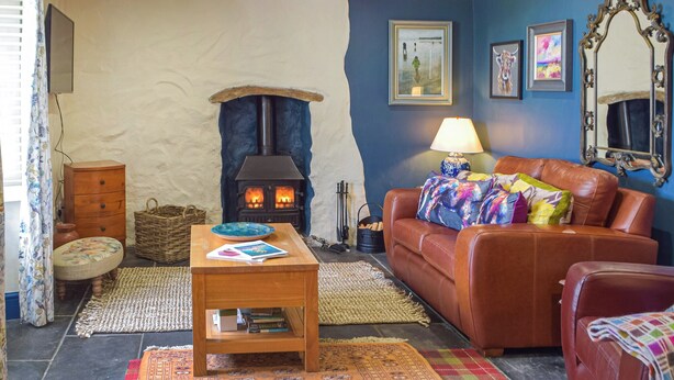 A cozy living room with a stone fireplace, a leather sofa, and a wooden coffee table. - Picked for its character, charm and gorgeous sea views from every window. (Berea, near St Davids)