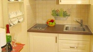 Una piccola cucina con mobili bianchi, un lavello in acciaio inossidabile e una ciotola di frutta sul piano di lavoro.