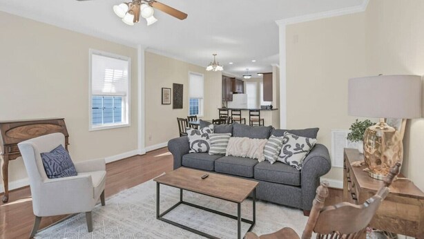 A living room with a grey sofa, a wooden coffee table, a white armchair, and a ceiling fan.