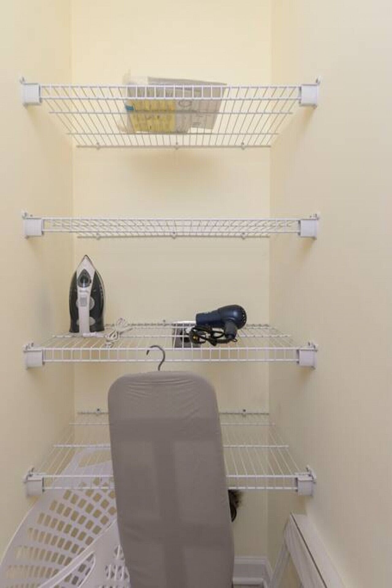 A laundry area with shelves holding an iron, a hairdryer, and a basket.