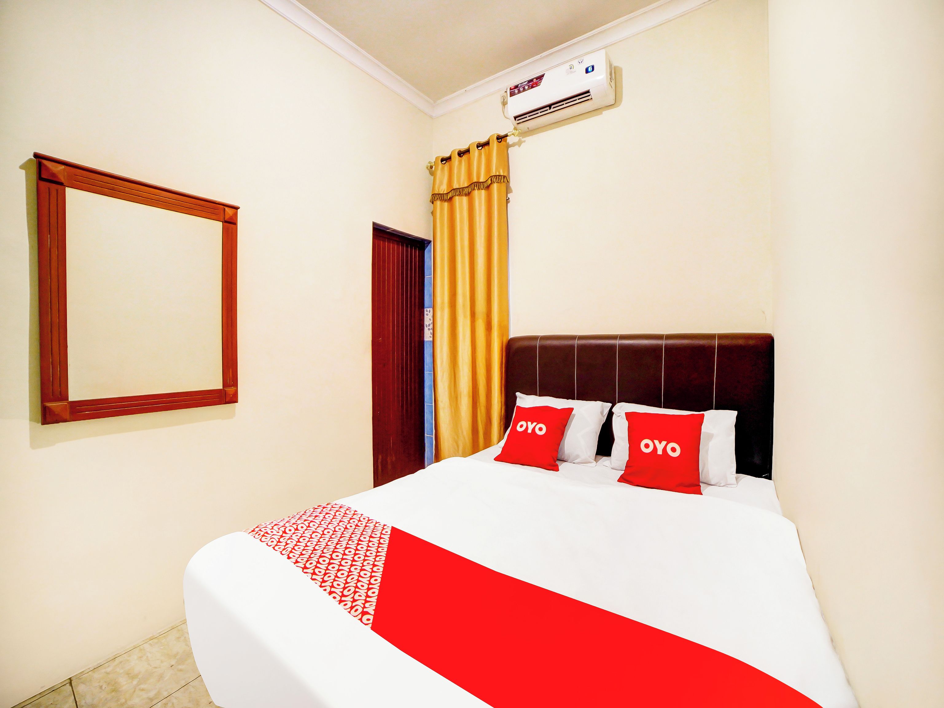 A hotel room with a bed, a mirror, a window with curtains, and an air conditioning unit.