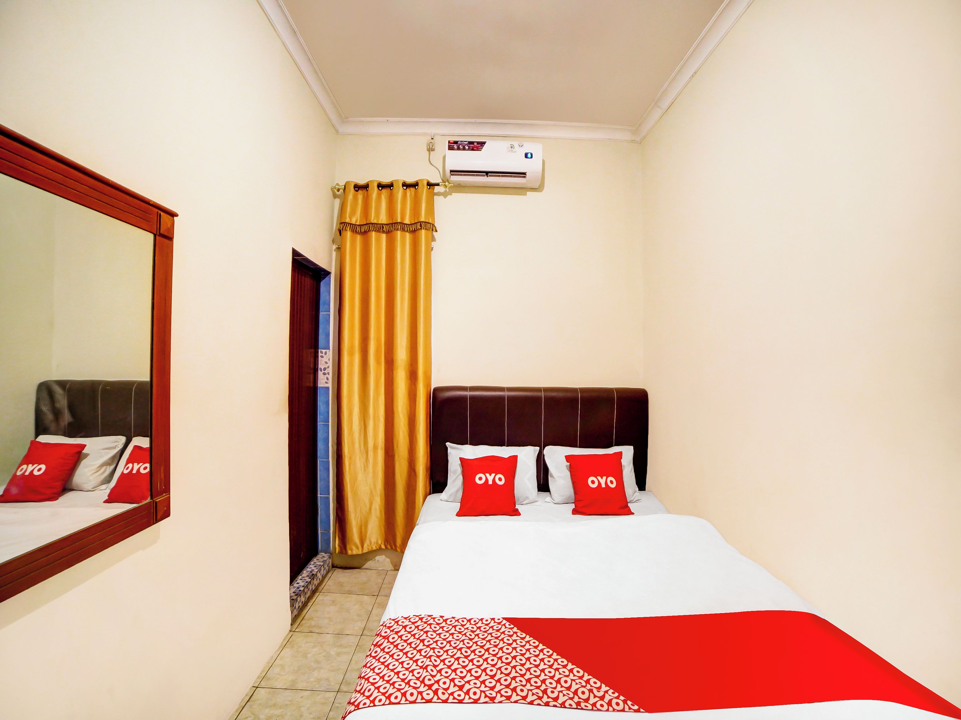 A hotel room with a bed, a mirror, a wall-mounted air conditioner, and a door leading to another room.