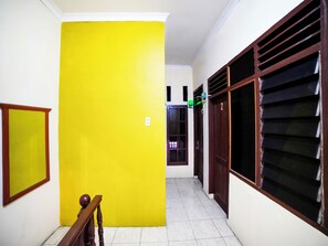 A hallway with a bright yellow door, a wooden bench, and a tiled floor. - OYO 91199 Felicia Homestay (Medan)