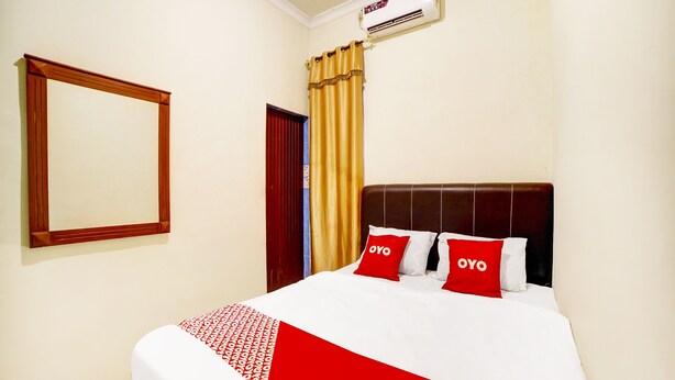 A hotel room with a bed, a mirror, a window with curtains, and an air conditioning unit. - OYO 91199 Felicia Homestay (Medan)