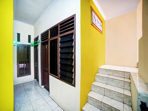 Un pasillo con suelo de baldosas, una puerta numerada y una escalera con un muro revestido.