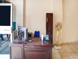 A wooden desk with a computer, a blue chair, a filing cabinet, and a standing fan. - OYO 91199 Felicia Homestay (Medan)