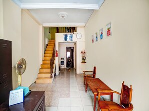 A hallway with a staircase, a dining area with a wooden table and chairs, a wall-mounted clock, and a calendar on a desk.