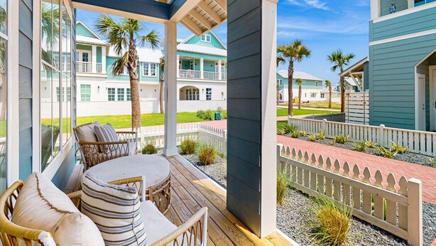A covered outdoor seating area with wicker furniture and a view of a coastal property with multiple buildings. - Serene newly built island home with outdoor pool, beach boardwalk & on-site golf (Port Aransas)
